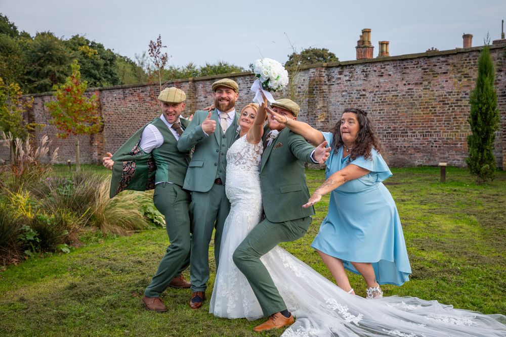 Bride and groom celebrate joyfully with wedding party members in a scenic walled garden.