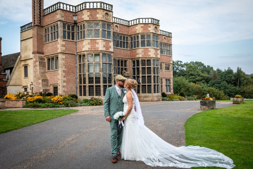 Bride and groom share a romantic kiss in front of a stunning historic manor house venue.