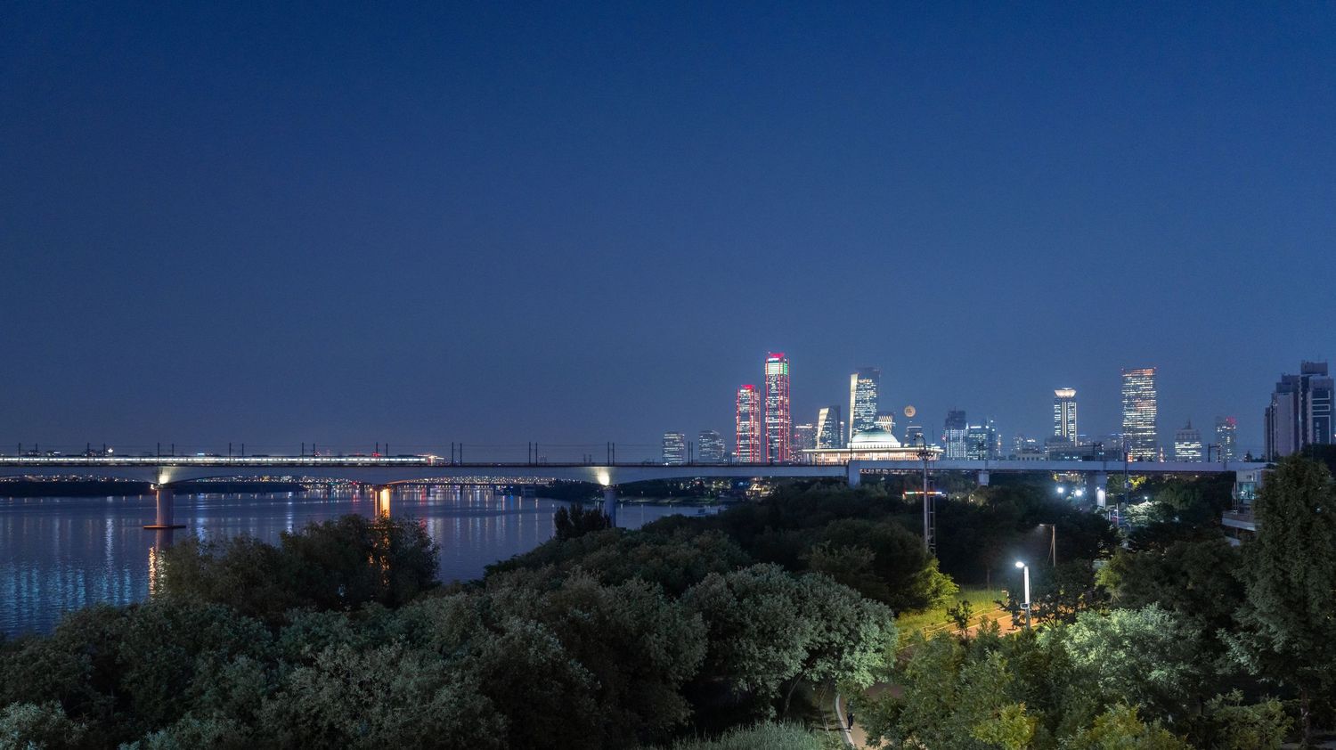 Night skyline panorama showing city lights against a deep blue sky.