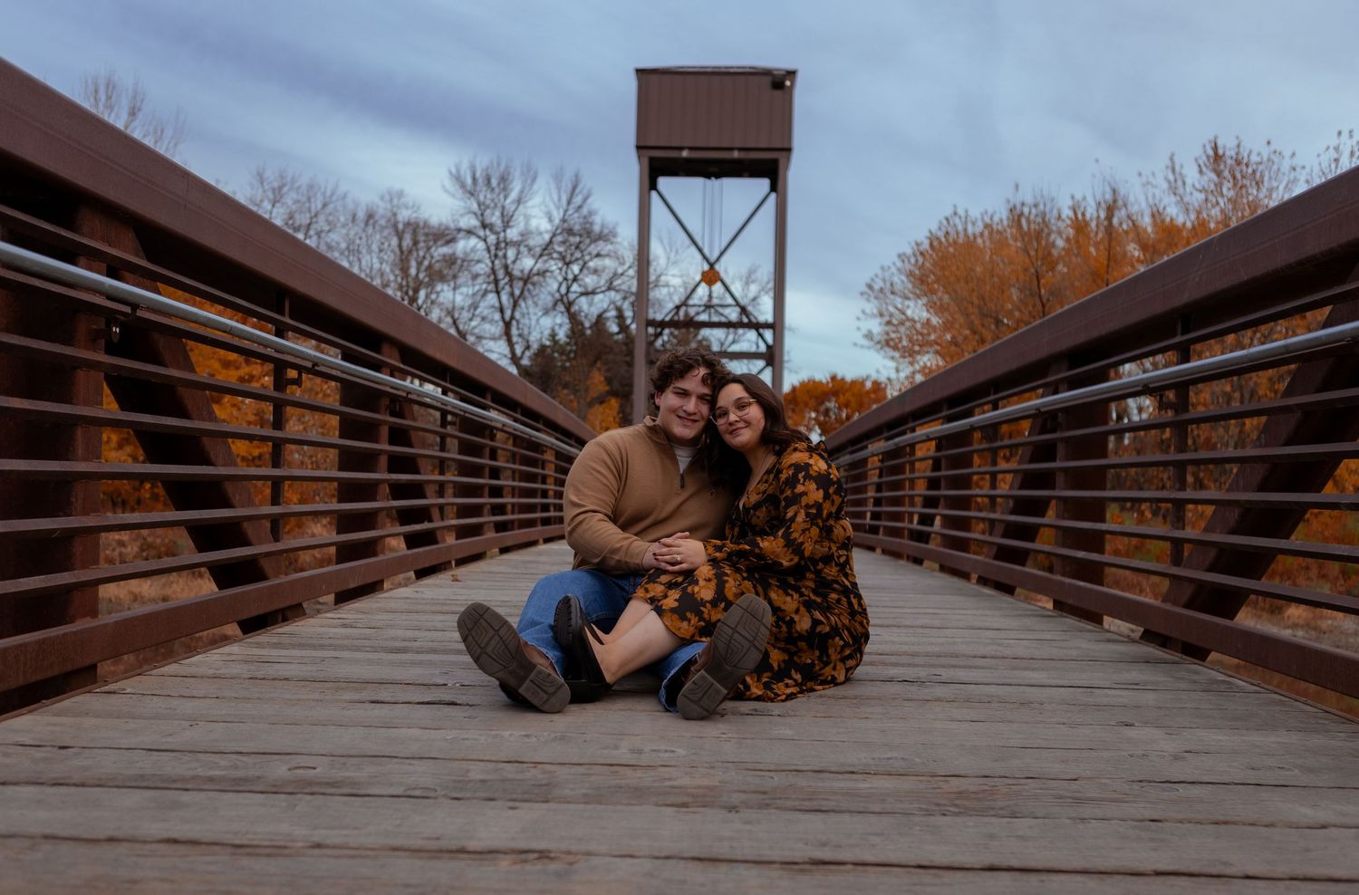 Couple relaxing on wooden bridge during outdoor photo session.