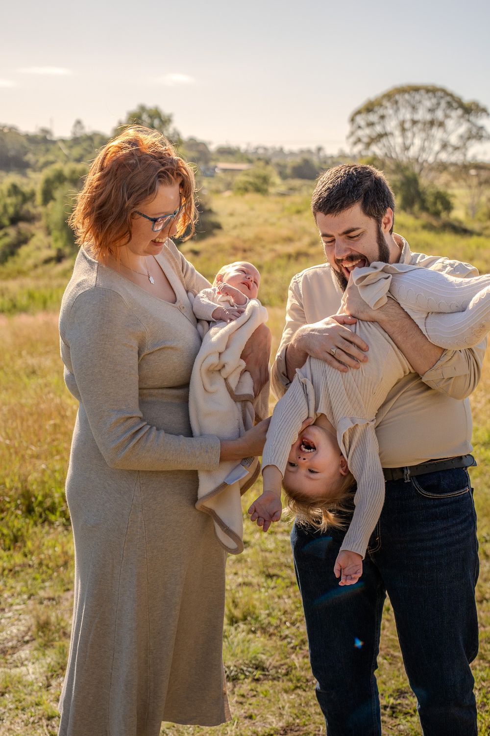 Family spending time together outdoors in a grassy field at sunset wearing matching beige outfits.