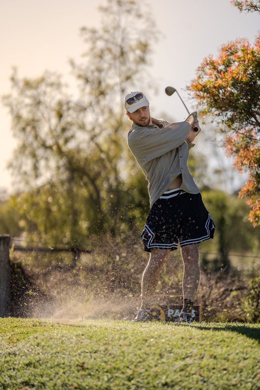 Golfer swings club on autumn course while kicking up dirt and grass during golden hour sunset.