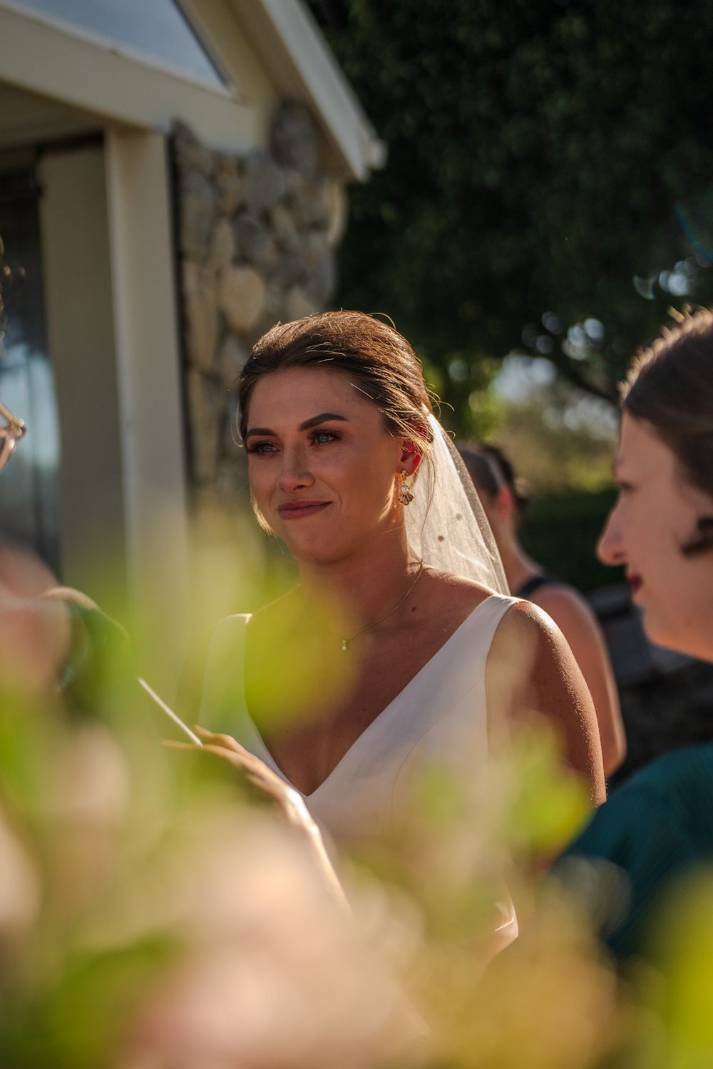Bride in white dress smiling during outdoor wedding ceremony.