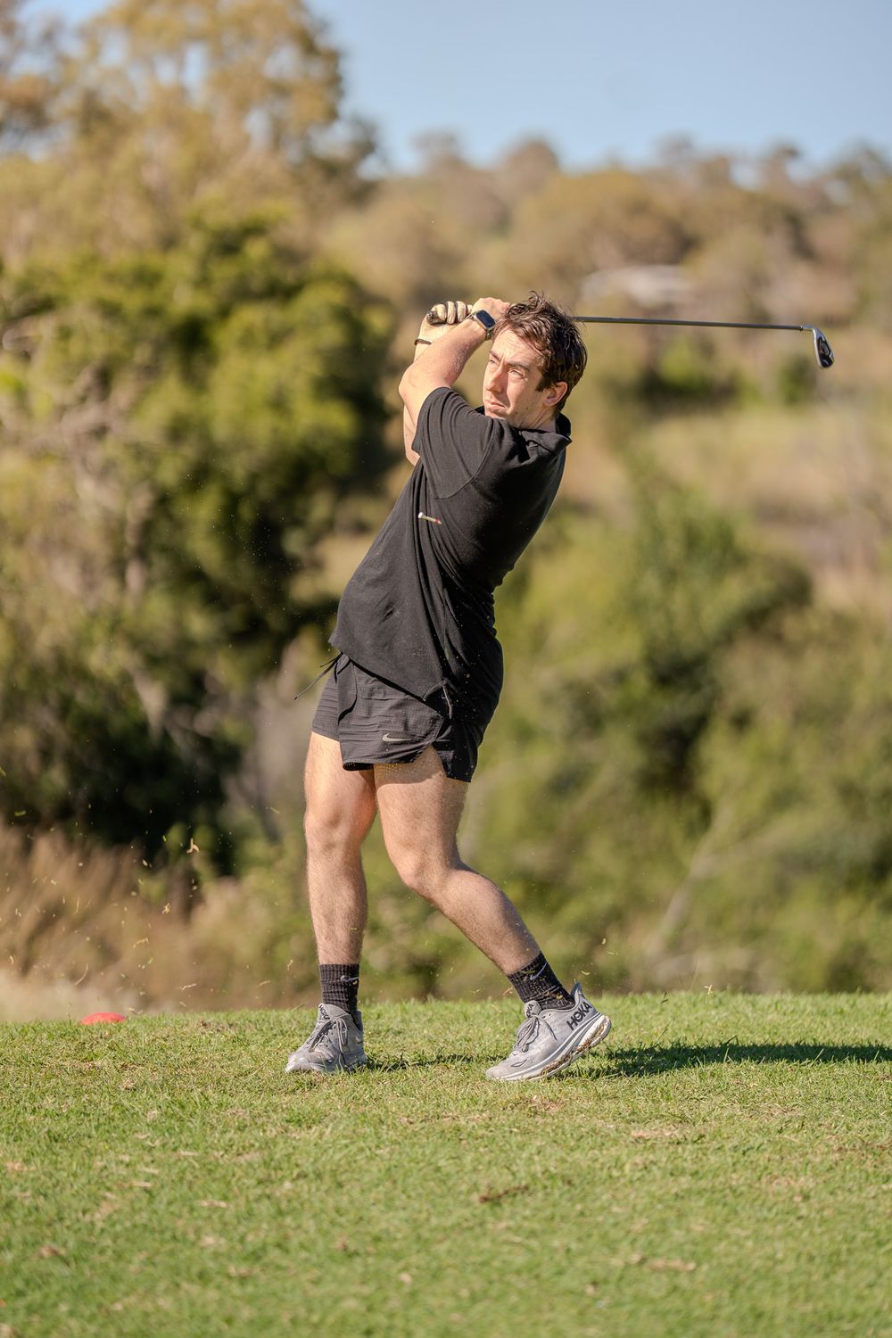 Golfer in black athletic wear follows through on swing with club on sunny golf course.