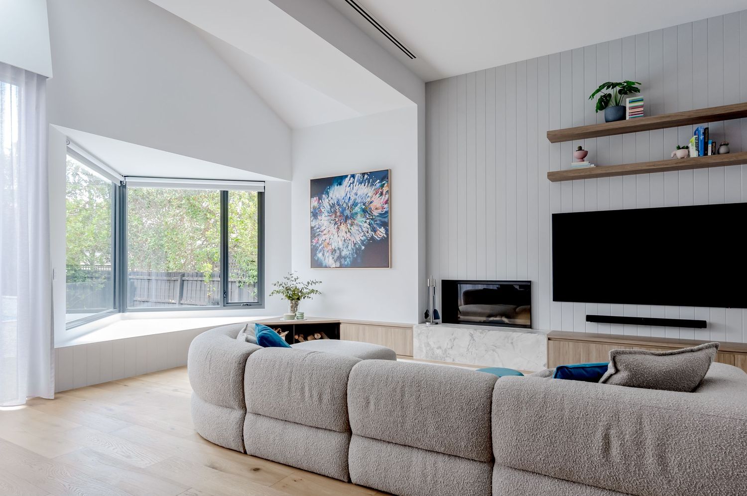 Contemporary living room with gray sectional sofa, large windows, and abstract blue artwork.