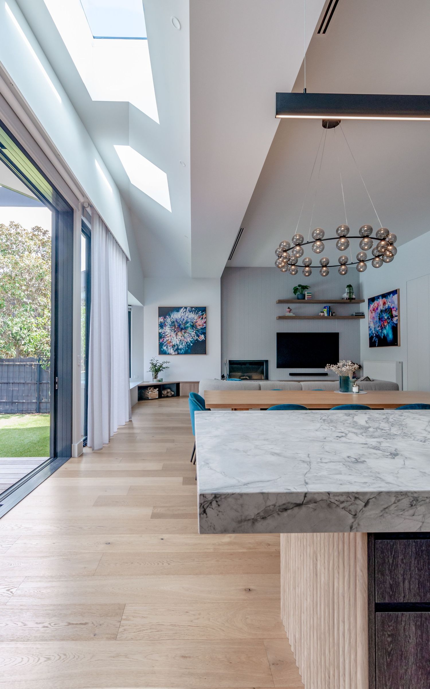 Bright living space with skylights, floor-to-ceiling windows, and marble kitchen island overlooking garden.