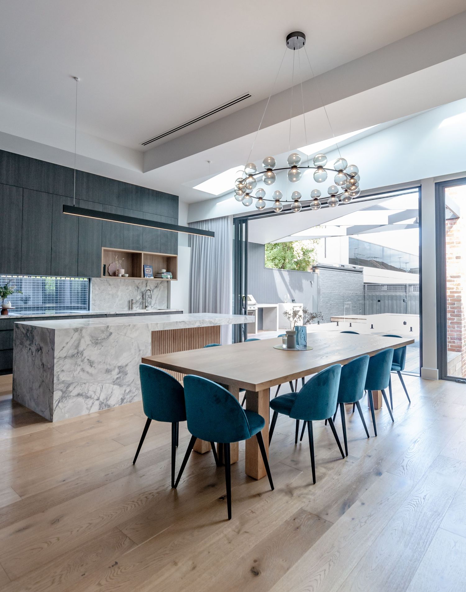 Modern dining area with blue velvet chairs, wooden table, and stunning circular glass chandelier.
