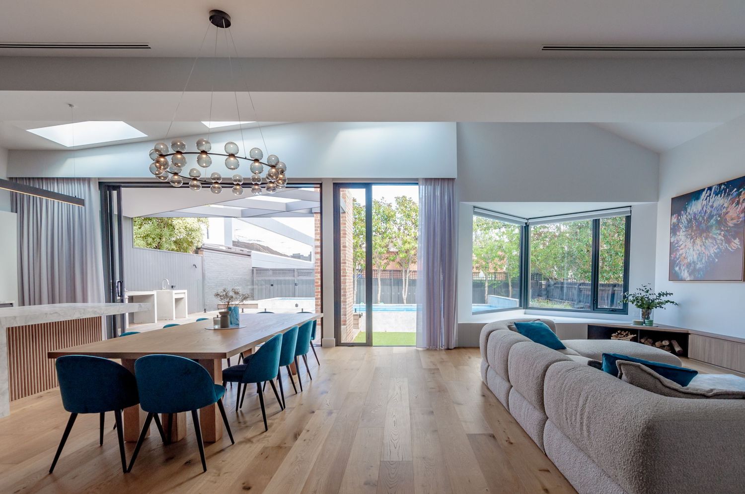 Open-plan living and dining space with high ceilings, skylights, and large windows overlooking garden.