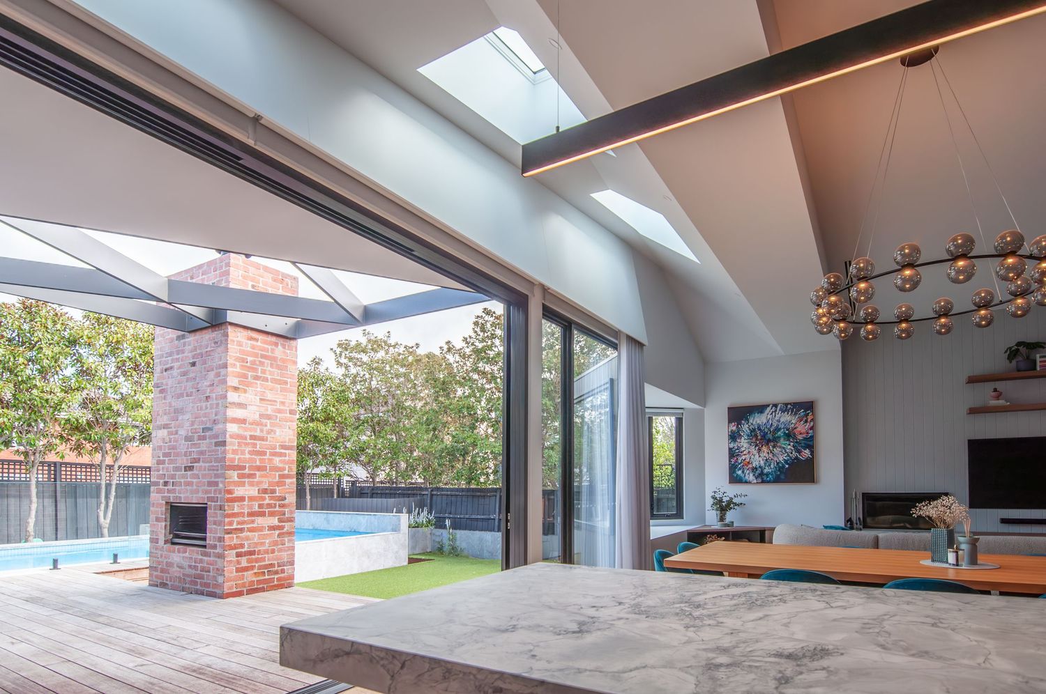 Indoor-outdoor living space with sliding glass doors, exposed brick chimney, and pool view.