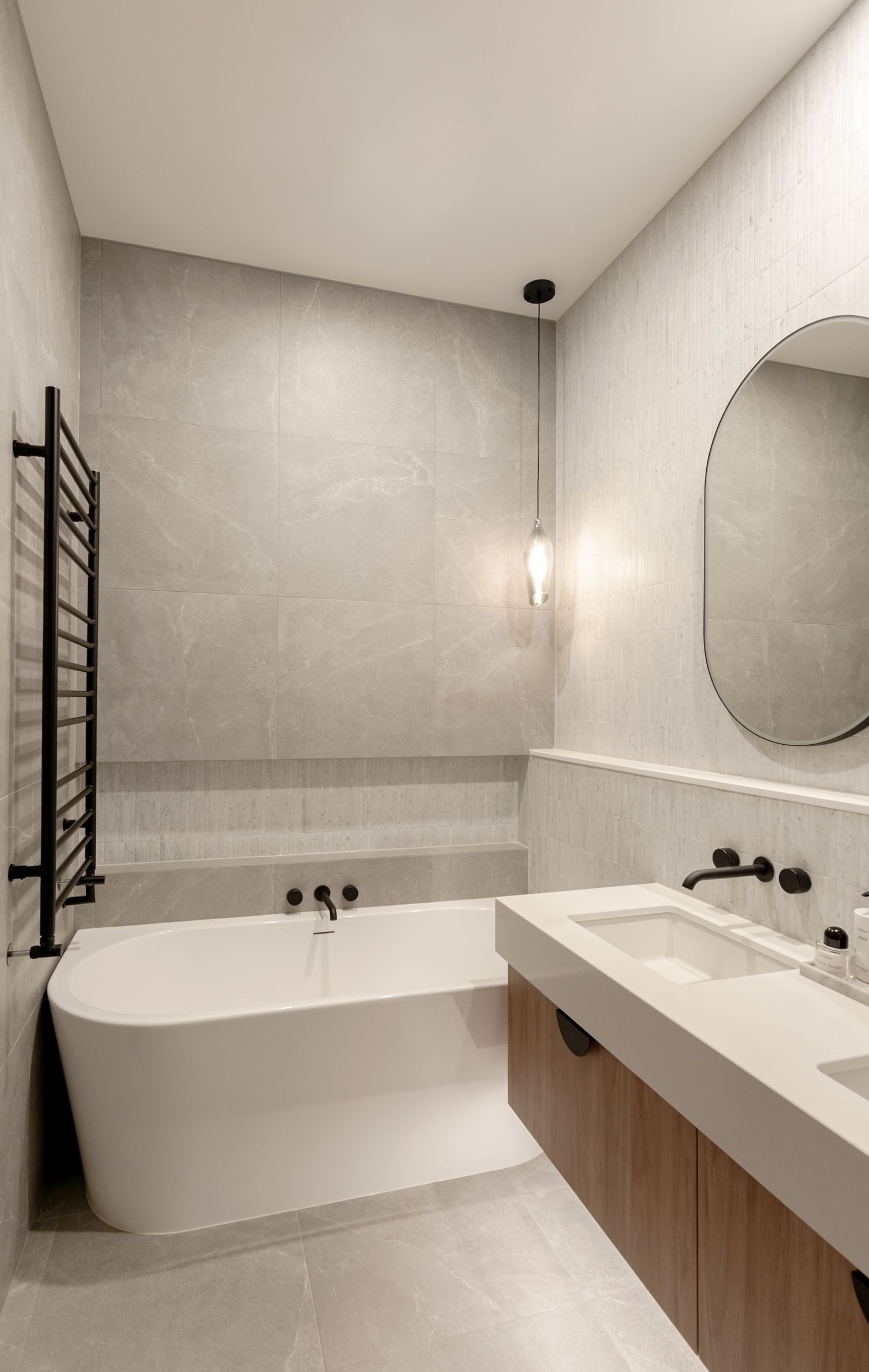 Minimalist bathroom featuring freestanding tub, wooden vanity, and round mirror with pendant lighting.