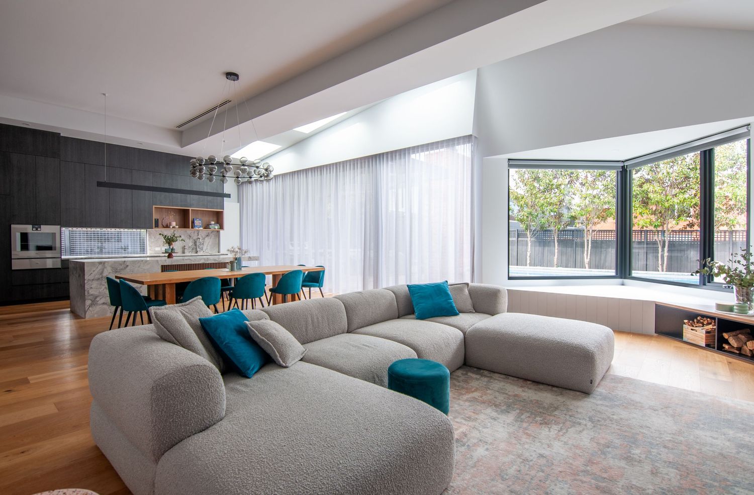 Modern living room with gray sectional sofa, blue accents, and floor-to-ceiling windows.