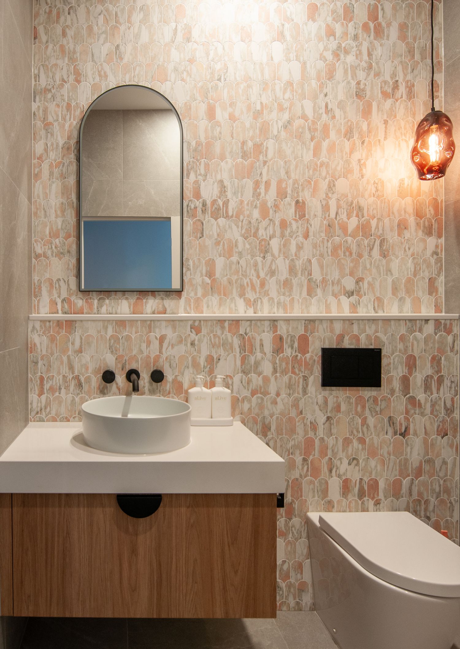 Powder room with peach textured wallpaper, vessel sink, and arched mirror design.