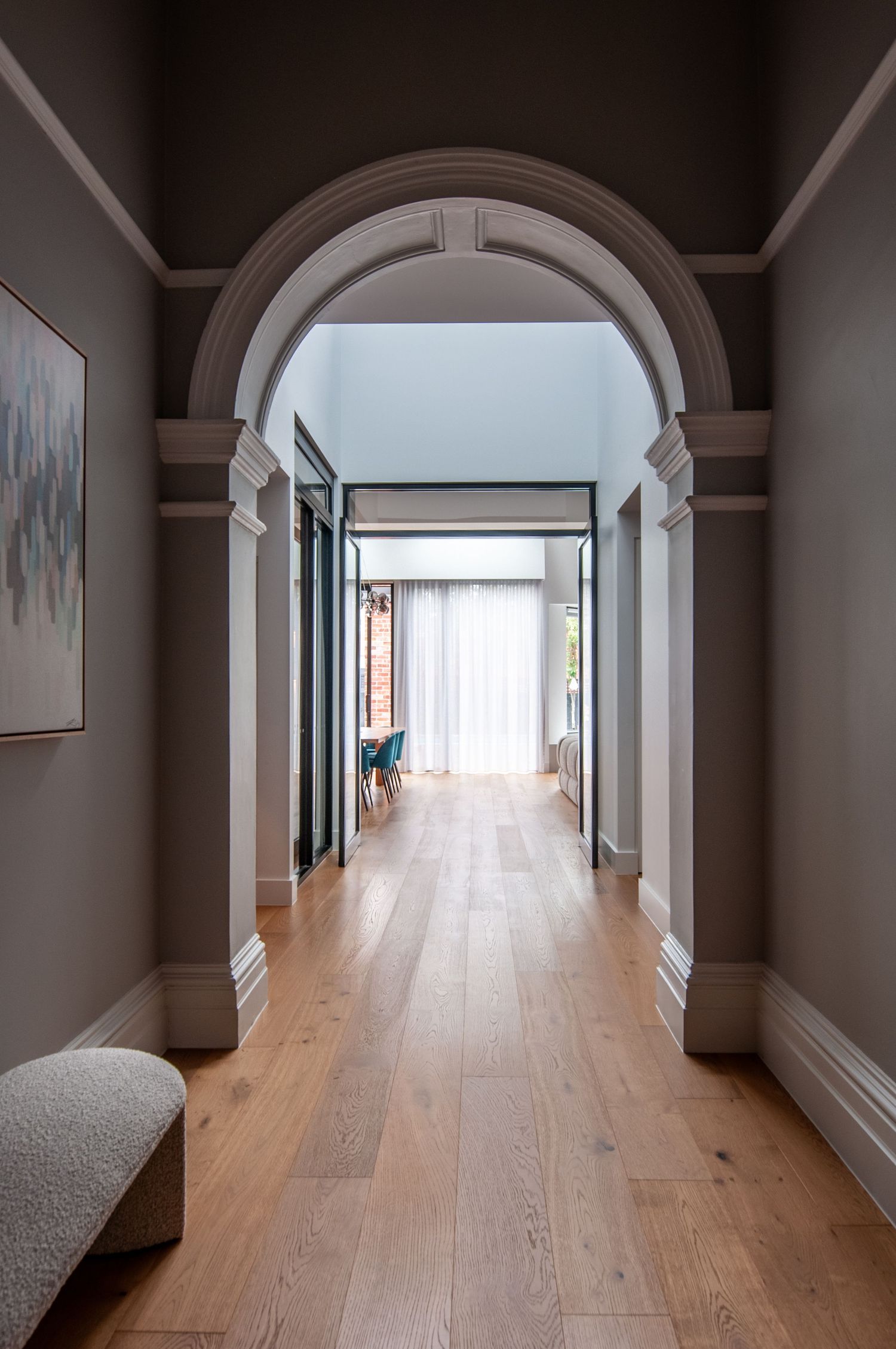Long hallway with arched doorway, wooden flooring, and gray walls leading to bright room.