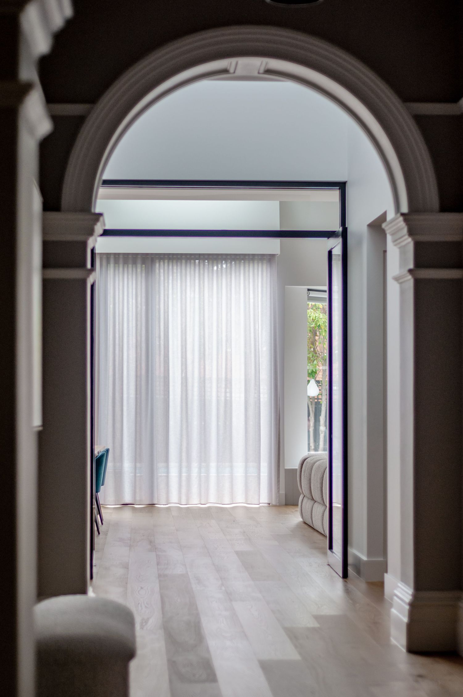 Contemporary hallway with arched entrance, white curtains, and light wooden flooring.