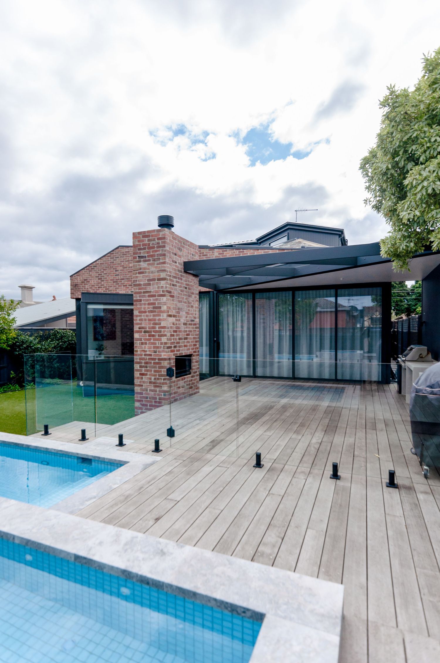 Modern house exterior with glass walls, brick facade, and swimming pool with timber deck.