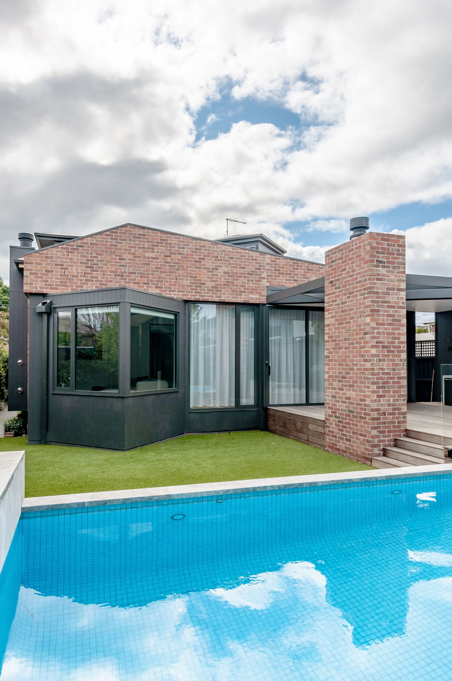 Modern brick house with dark trim and floor-to-ceiling windows overlooking swimming pool.