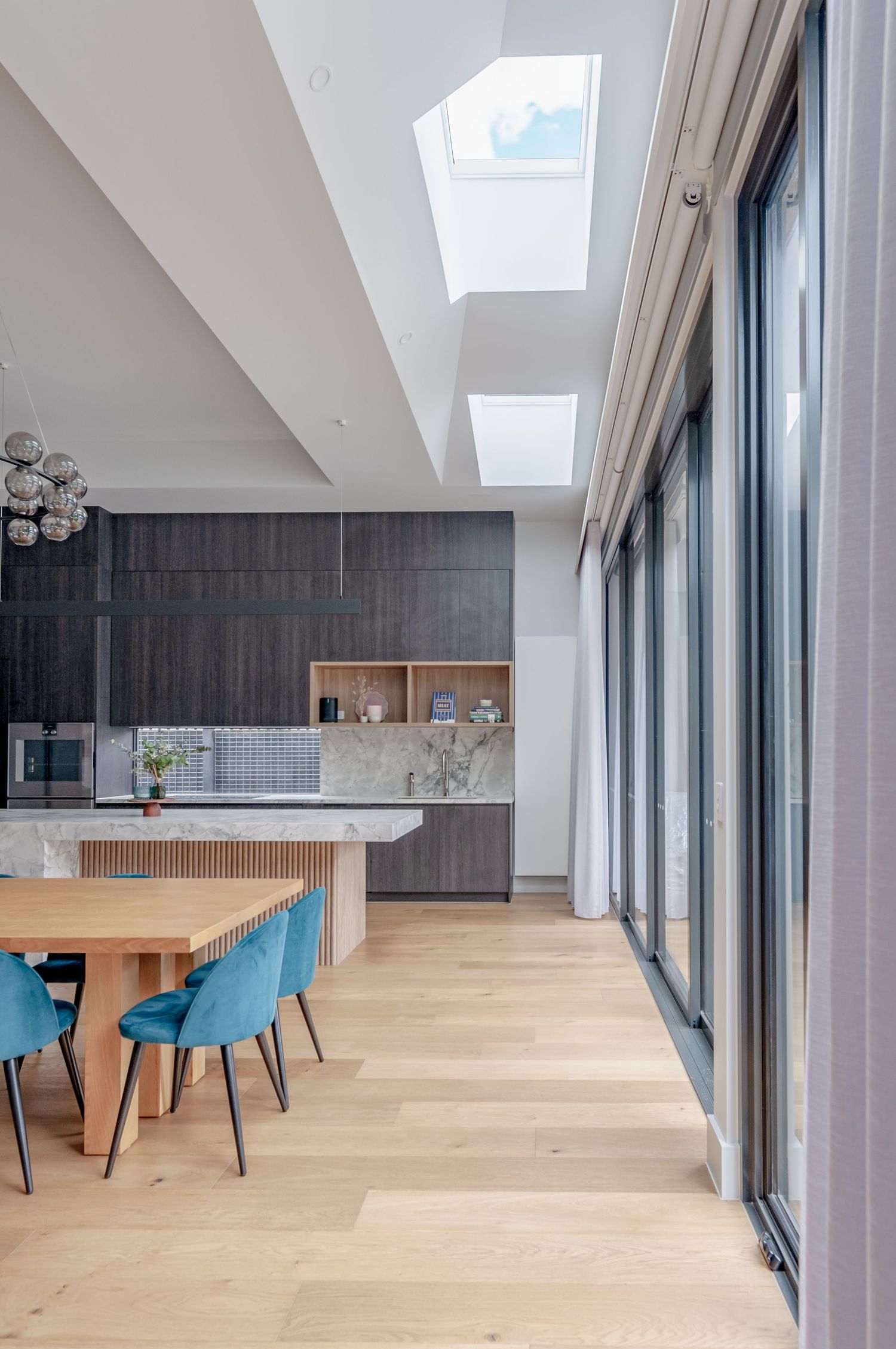 Bright dining area with skylights, blue chairs, and floor-to-ceiling windows overlooking exterior.