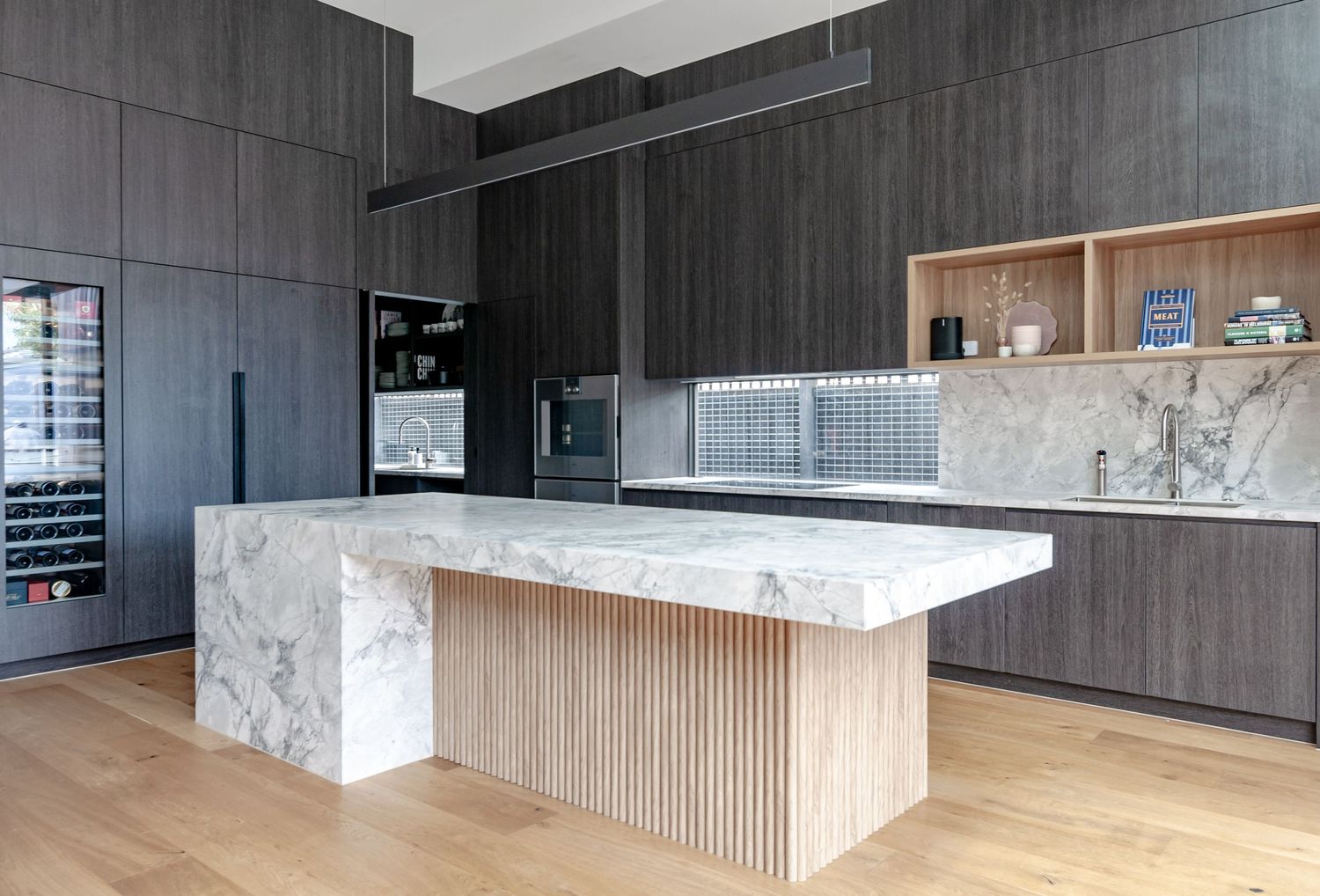 Luxurious kitchen featuring dark wood cabinets, marble island, and wooden slat details.