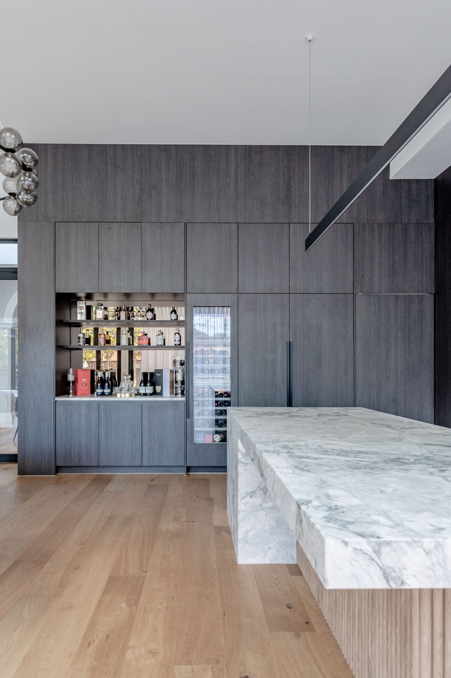 Modern kitchen with built-in bar area, marble countertops, and dark wood cabinetry.