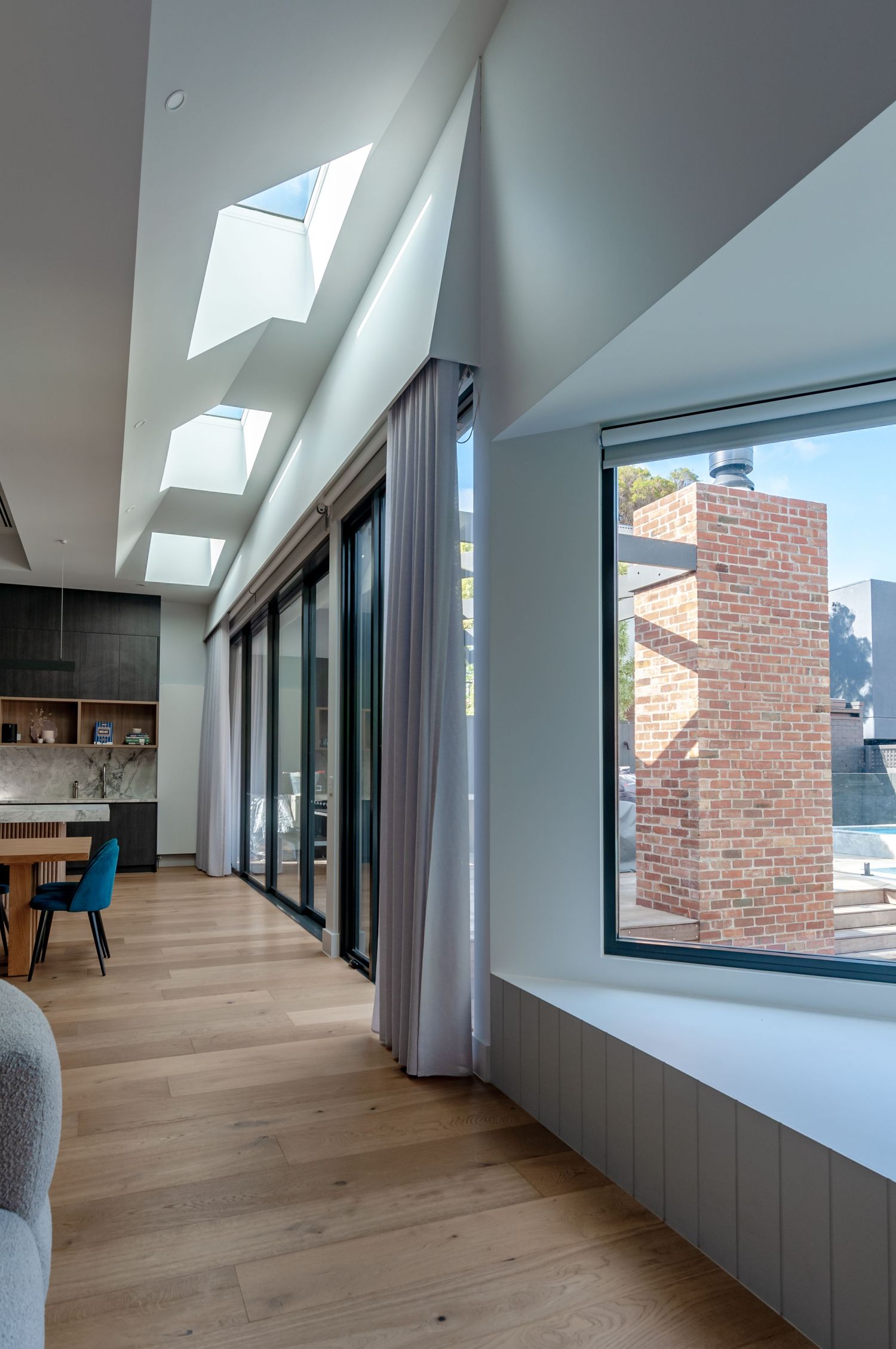 Interior space with multiple skylights, floor-to-ceiling windows, and view of brick building exterior.