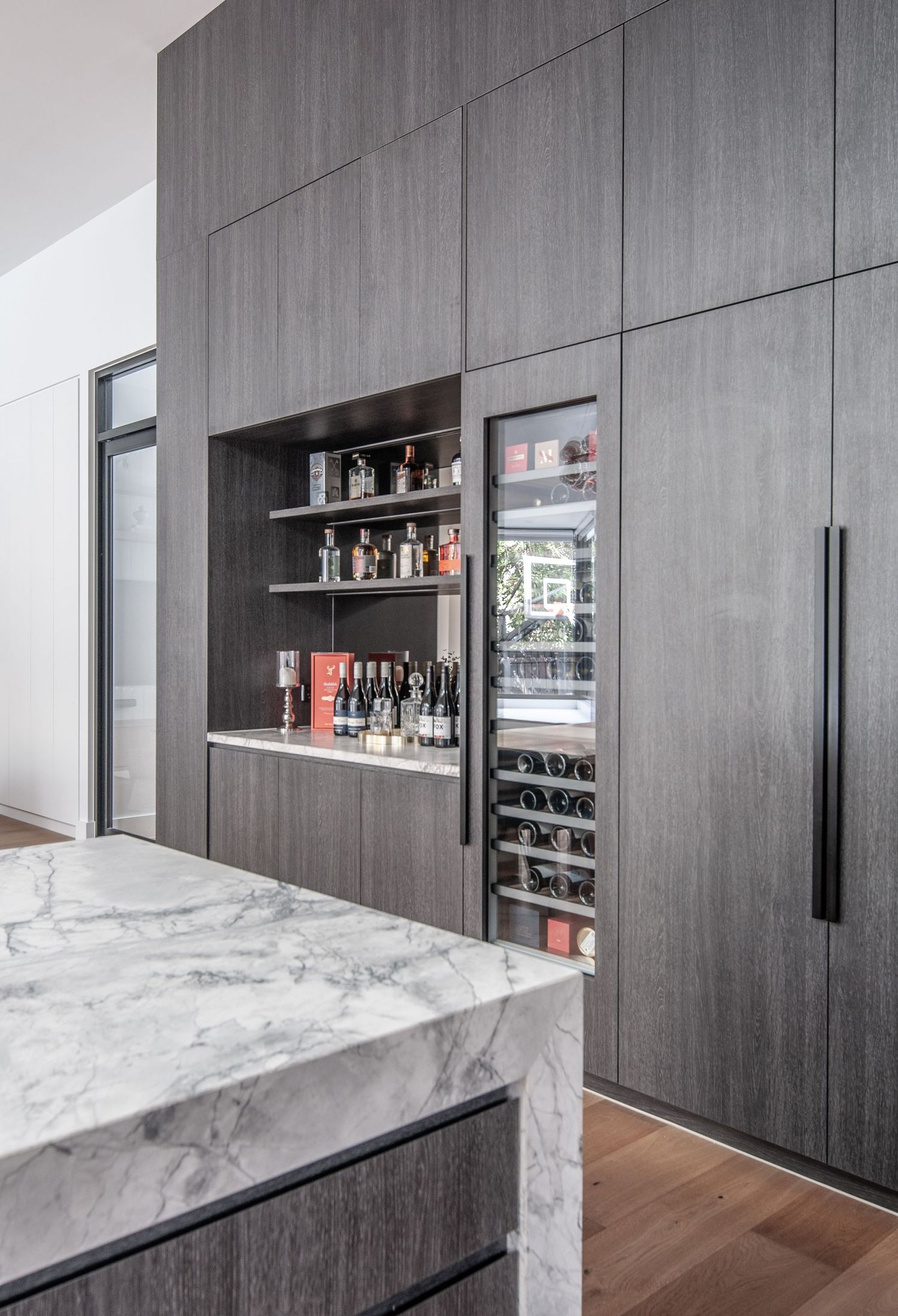 Modern kitchen featuring dark wood cabinetry, built-in wine storage, and floating shelves displaying liquor bottles.
