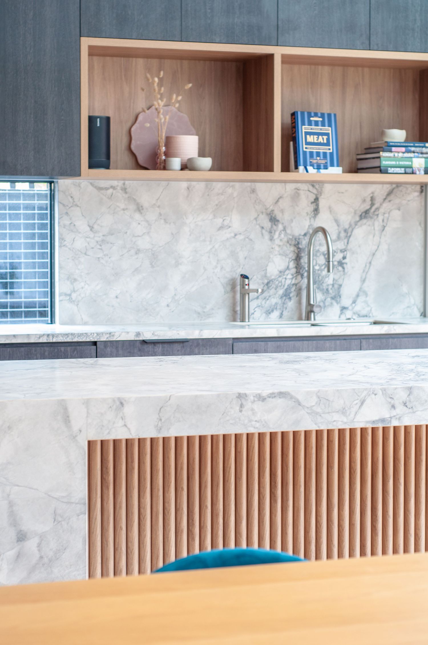 Modern kitchen interior featuring marble countertops, wooden slat details, and built-in shelving with decorative items.