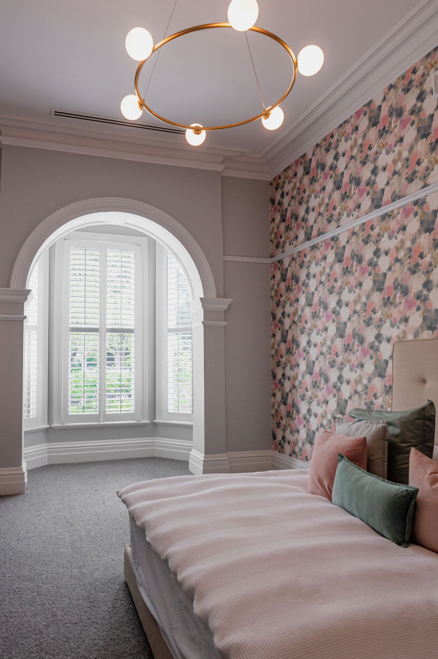 Elegant bedroom with arched window, floral wallpaper, and circular pendant light fixture.