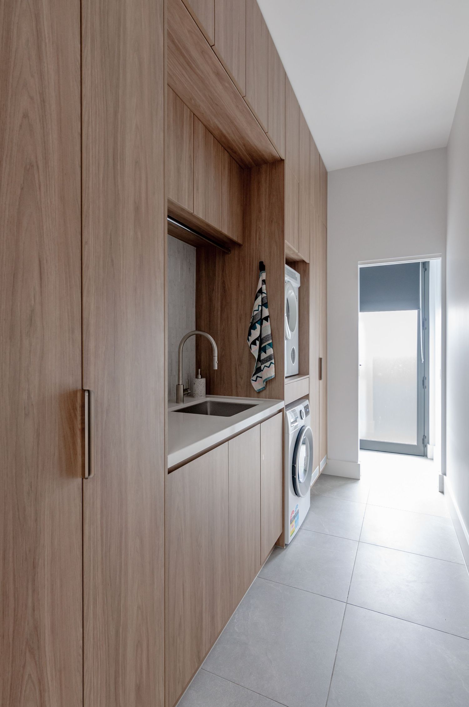 Sleek laundry room with built-in wooden cabinetry and modern appliances in a narrow hallway.