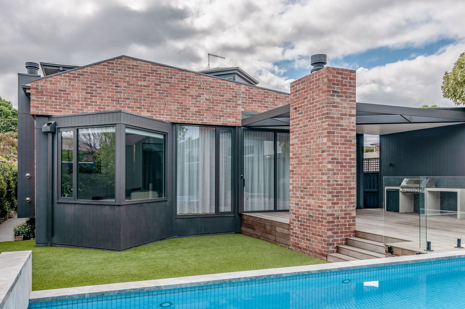 Modern brick house exterior with pool and glass walls featuring contemporary architectural design.