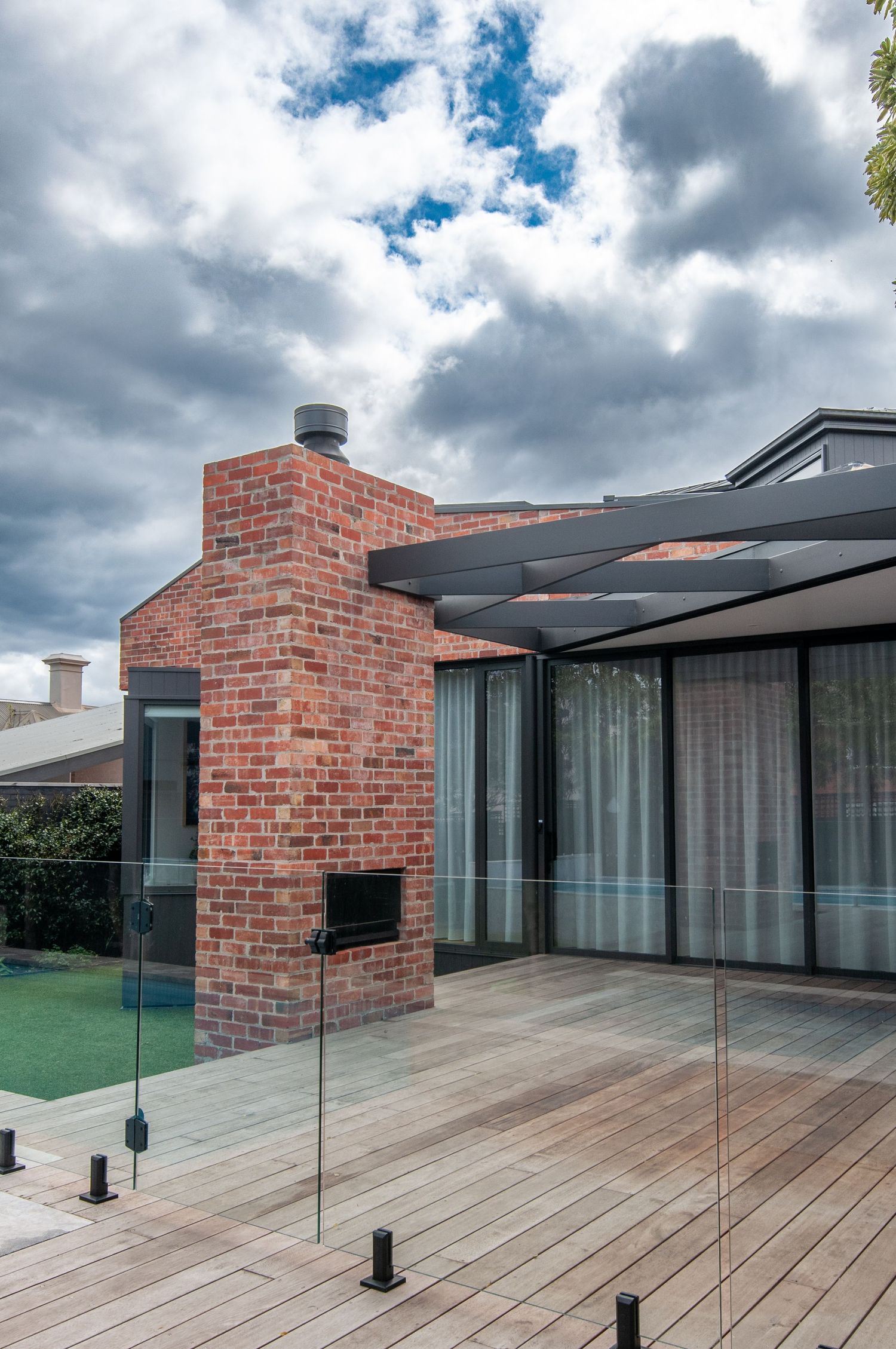 Contemporary brick house with glass balustrade and wooden deck overlooking swimming pool.