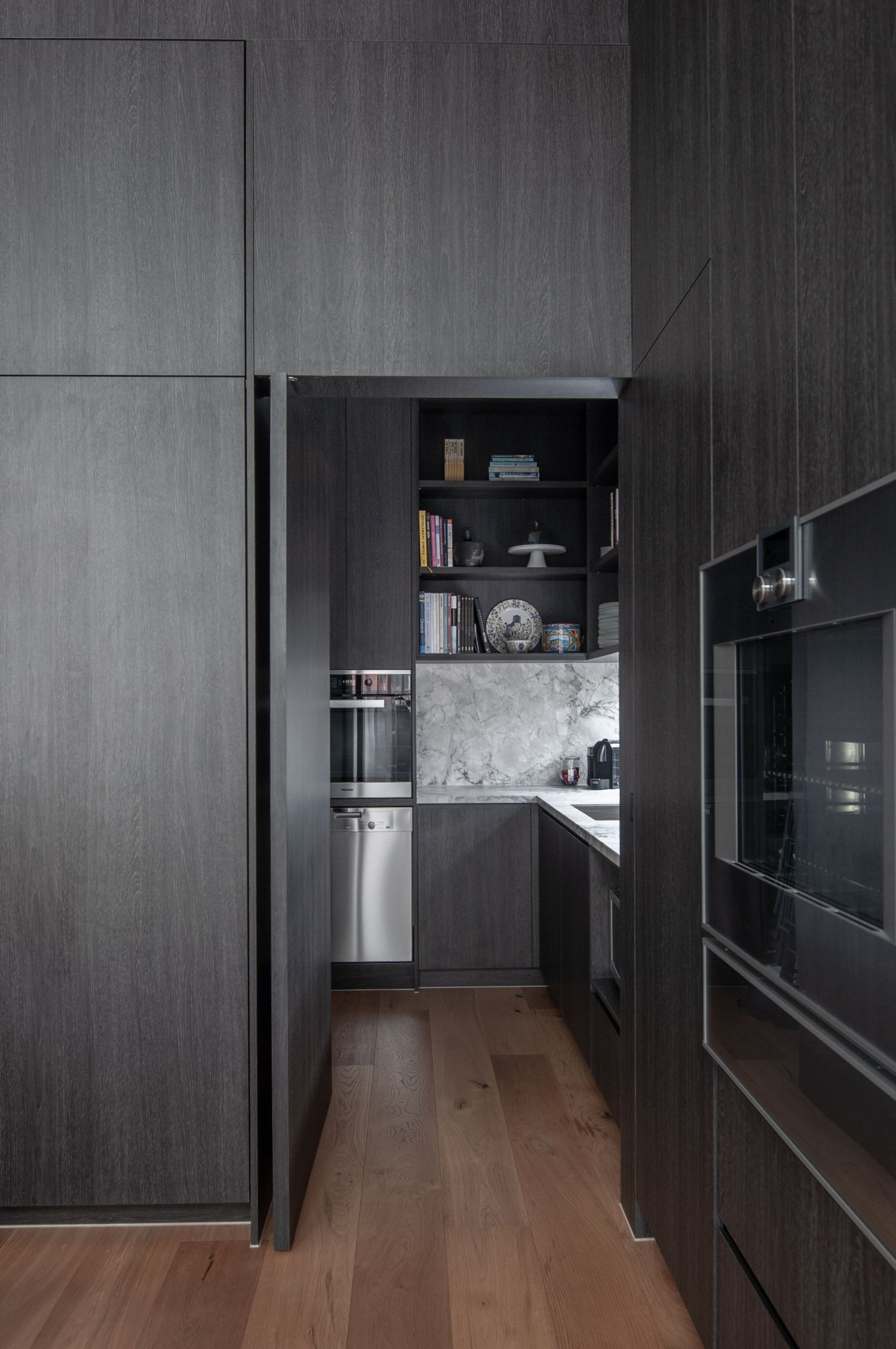Dark wood paneled kitchen hallway with built-in appliances and hardwood flooring.