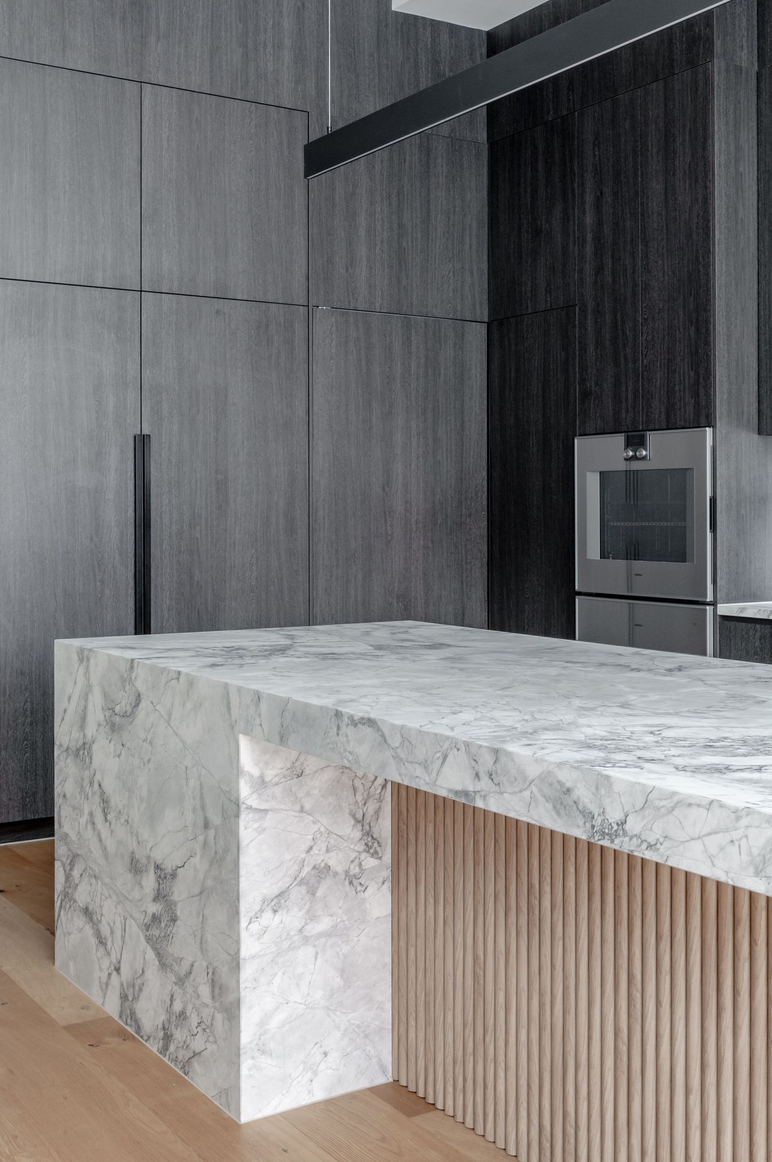 Luxury kitchen island with marble waterfall countertop and wooden slat detail.