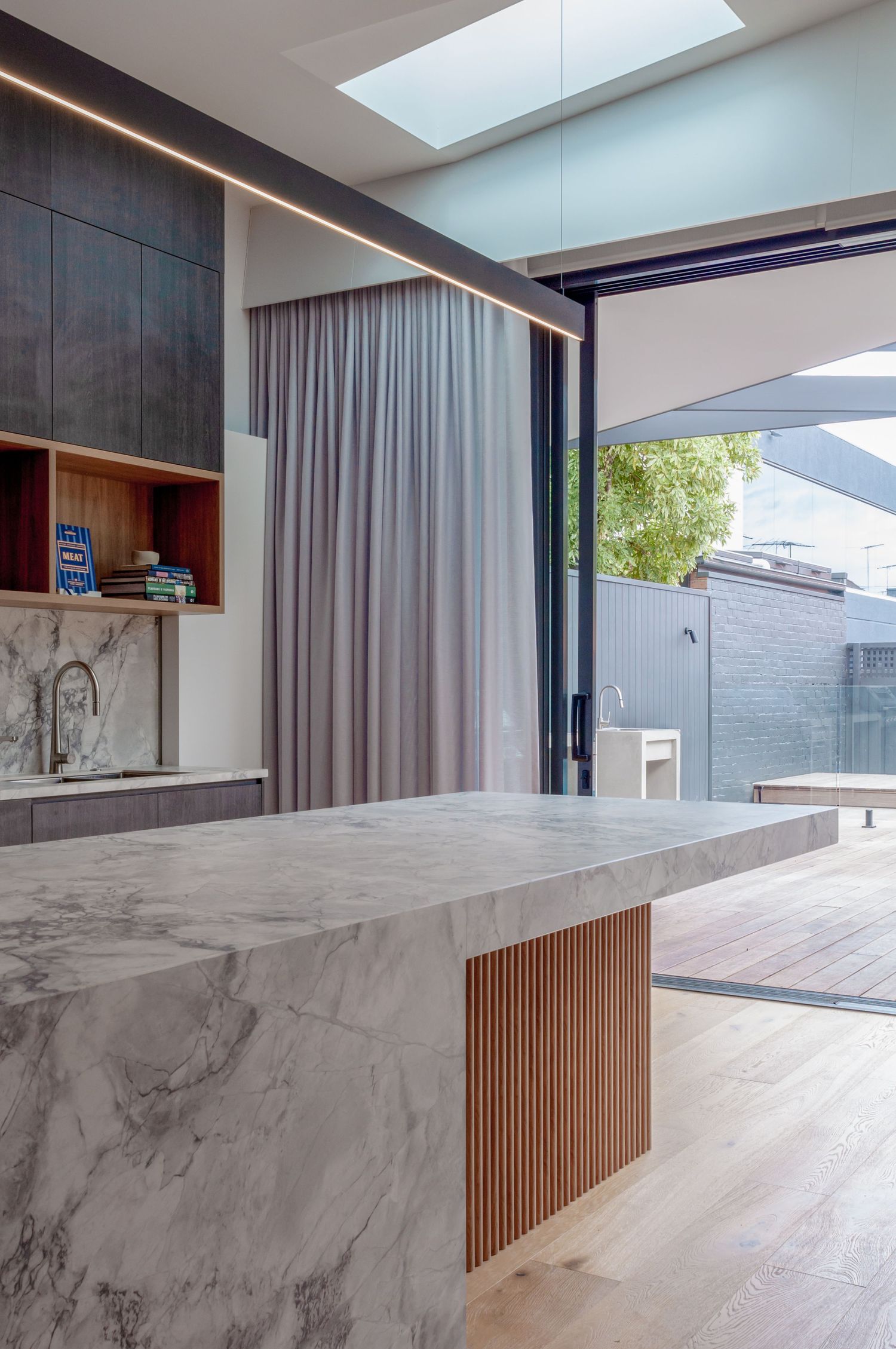 Modern kitchen with marble island, wooden accents, and indoor-outdoor flow through sliding doors.