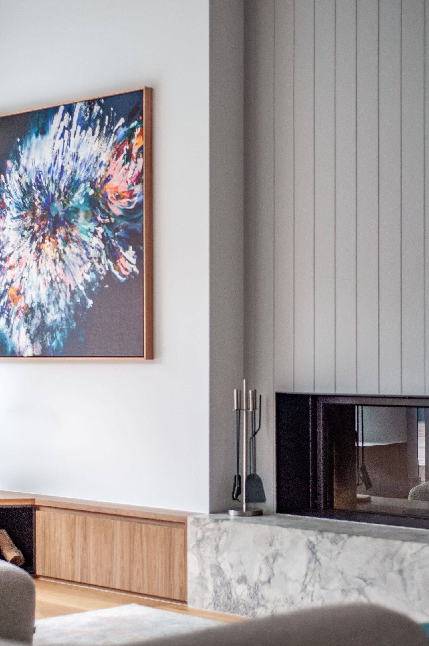 Living room detail featuring blue abstract artwork, marble fireplace, and wooden storage cabinet.