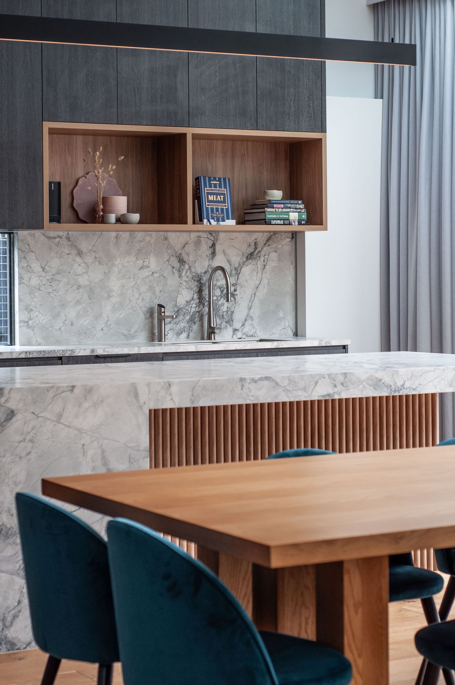 Dining area with marble kitchen counter, wooden shelving, and teal velvet chairs.