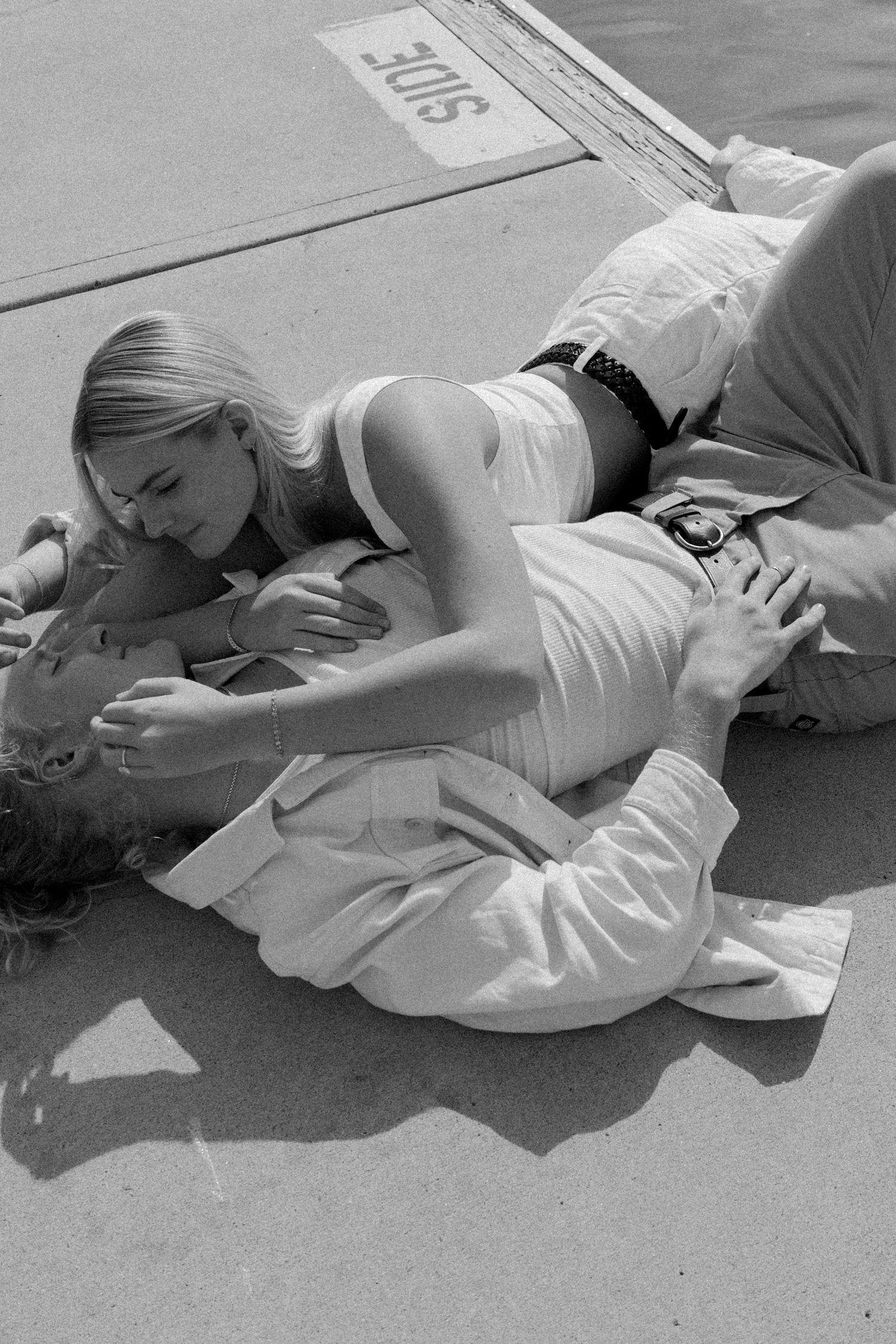 Two people lying close together on a dock in casual summer attire.