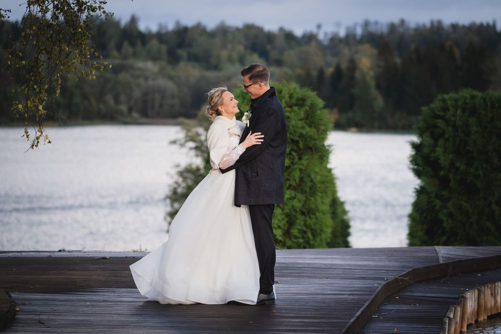 Wedding couple embracing on wooden dock with serene lake in background.