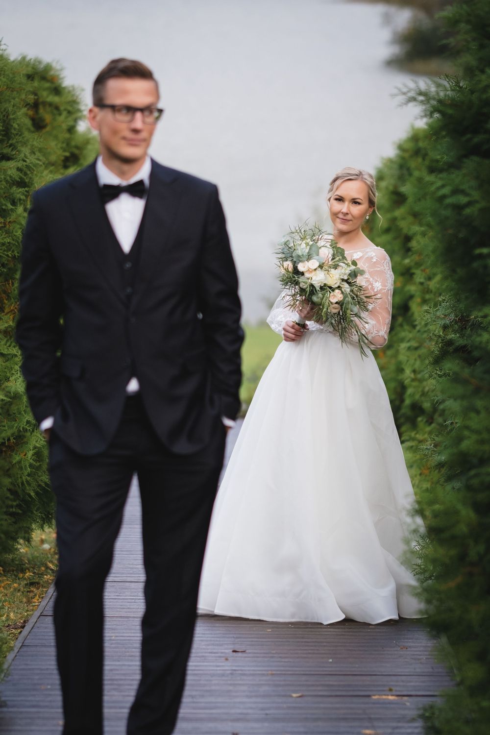 Wedding portrait on wooden boardwalk with couple among green hedges.