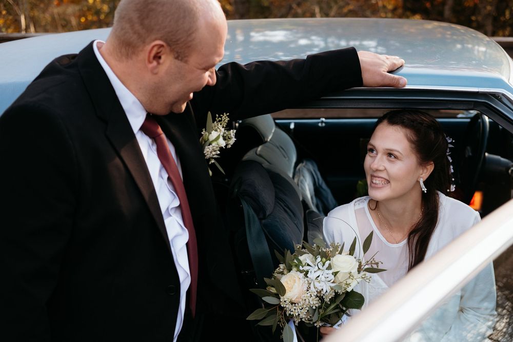 A couple shares an intimate moment on their wedding day near a car in winter.