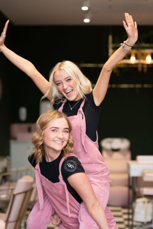 Two employees in pink aprons pose cheerfully together at a restaurant or cafe.