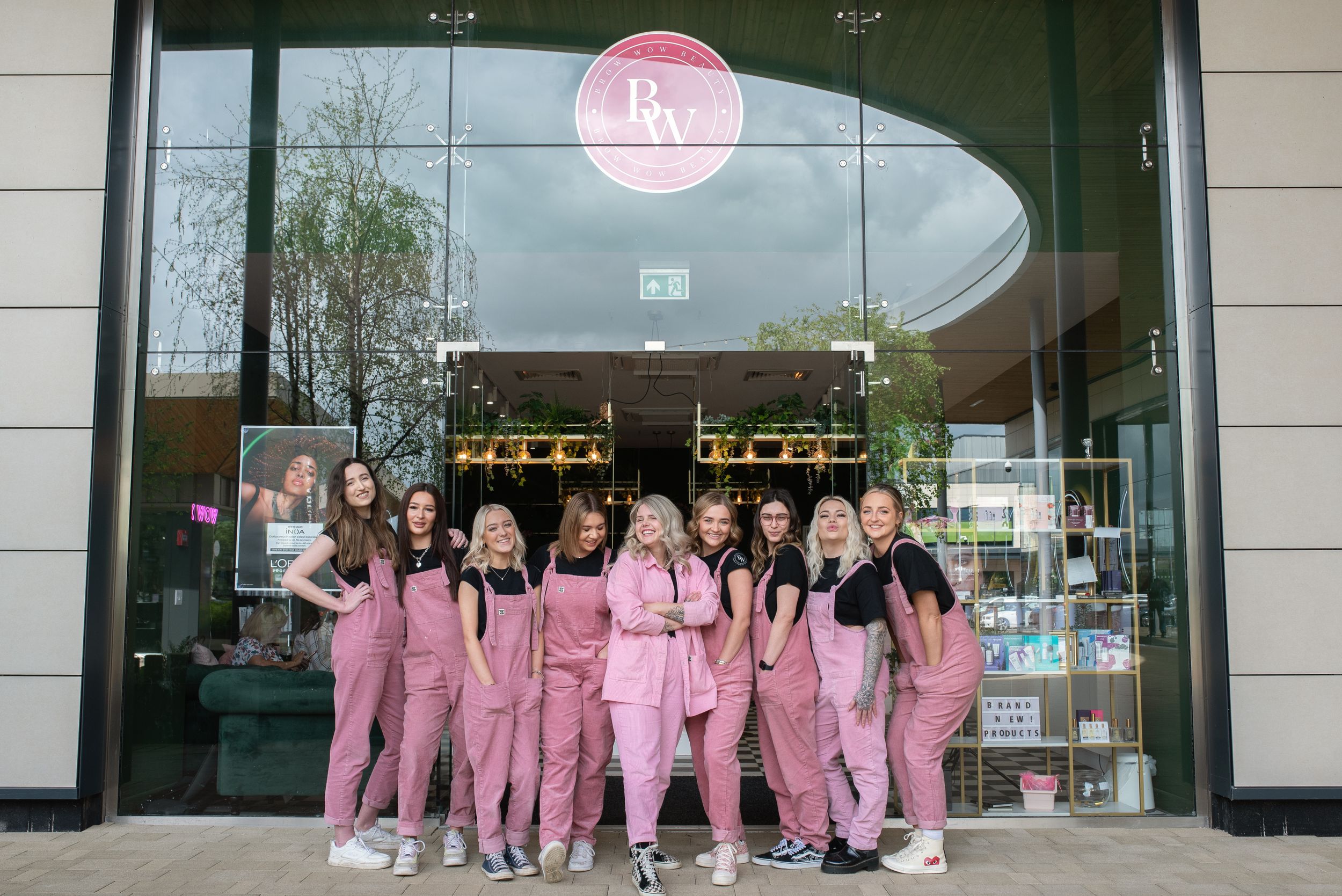 A group of staff members in pink uniforms pose together outside a modern storefront.