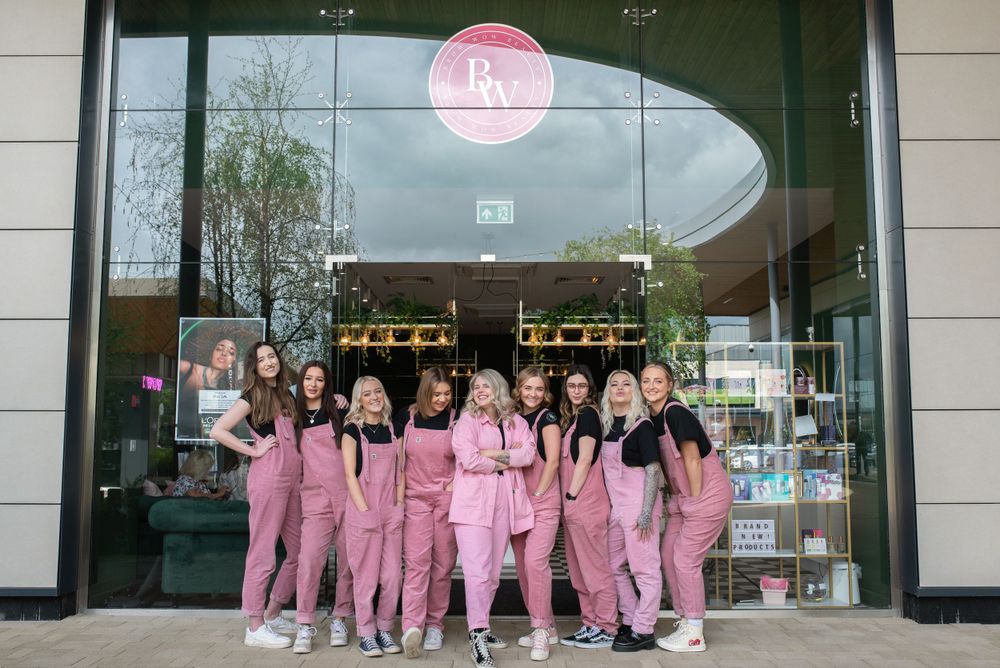 A group of staff members in pink uniforms pose together outside a modern storefront.