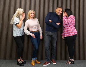 Four people lean against a brown striped wall while laughing and sharing a lighthearted moment together. Brand photos for company