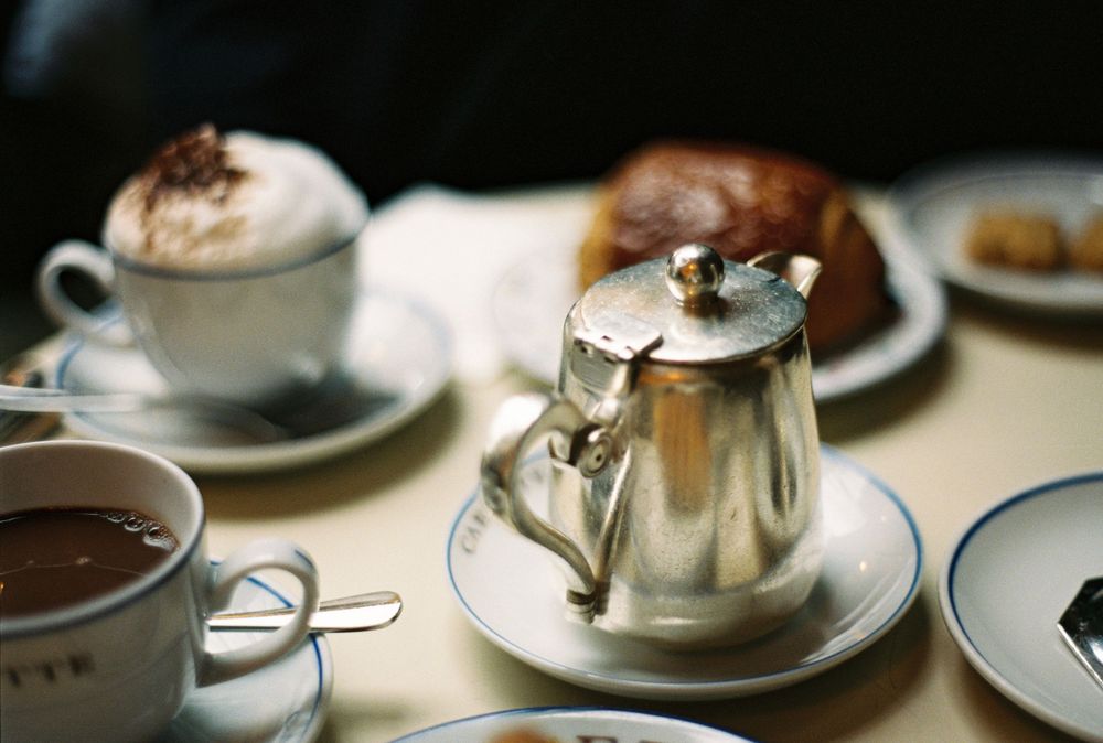 A vintage silver teapot with hot chocolate and pastries on a cafe table in Paris.