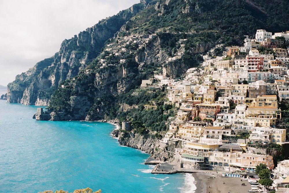 Colorful buildings cascade down steep cliffs toward the turquoise waters of Positano on the Amalfi Coast, Italy.
