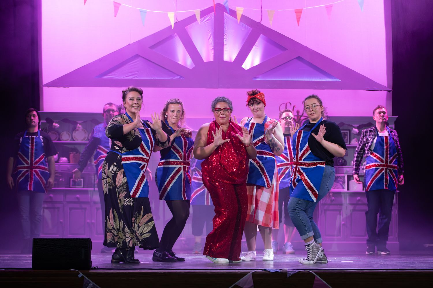 Colorful stage performance with dancers in Union Jack costumes under purple theatrical lighting.