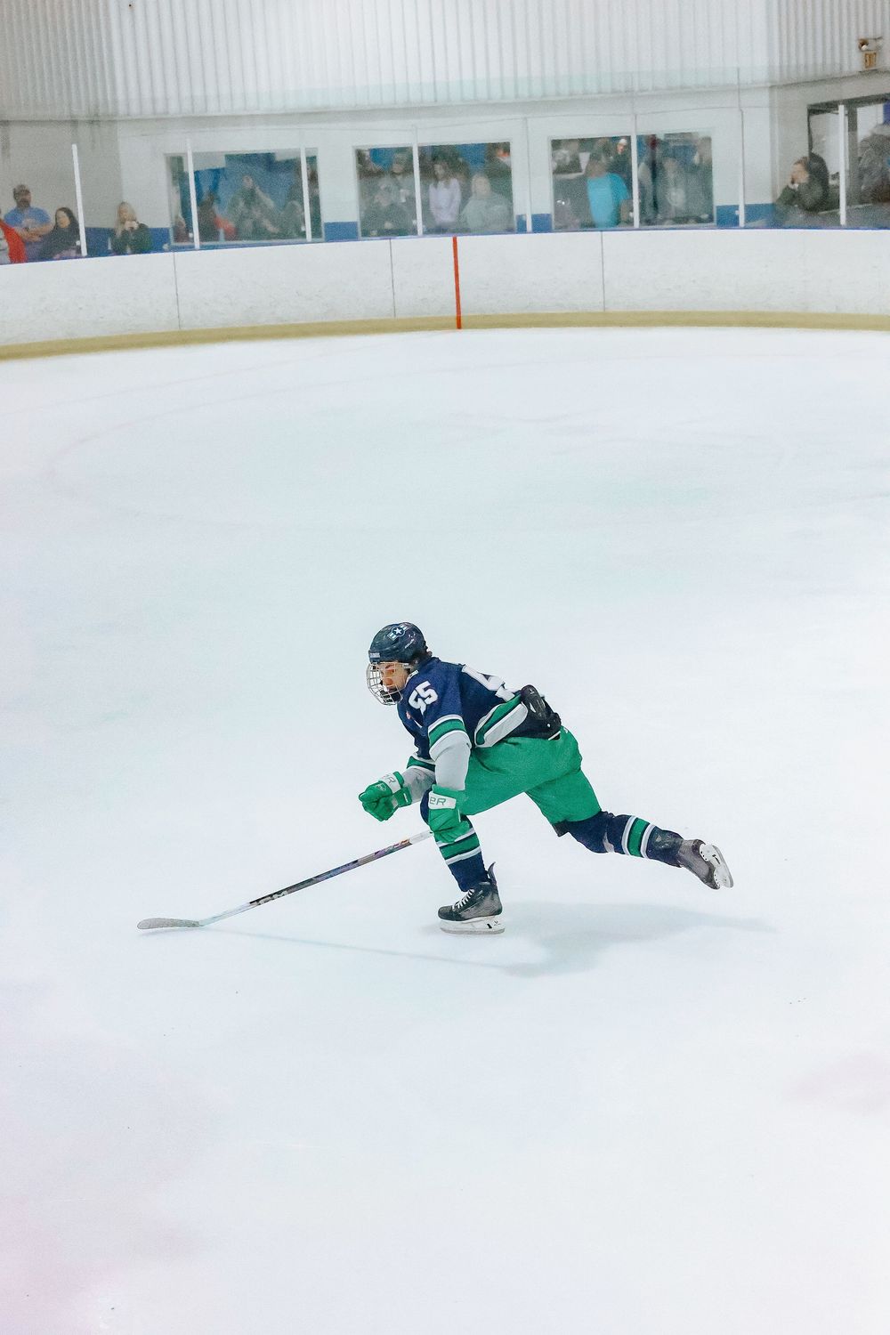 Hockey player in green jersey falls on ice during game while opponent in blue uniform looks on.