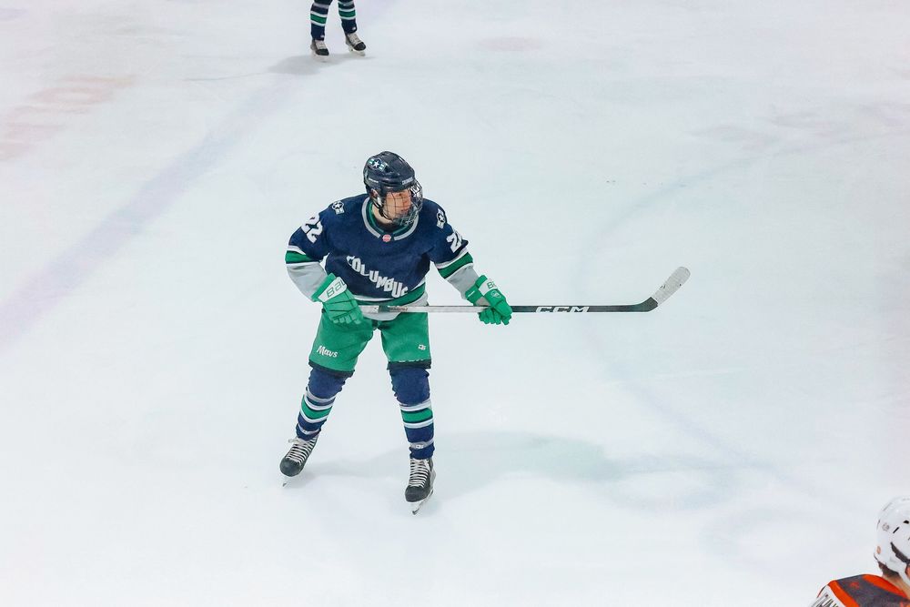 Hockey player in a teal jersey skates on ice with stick extended during gameplay.