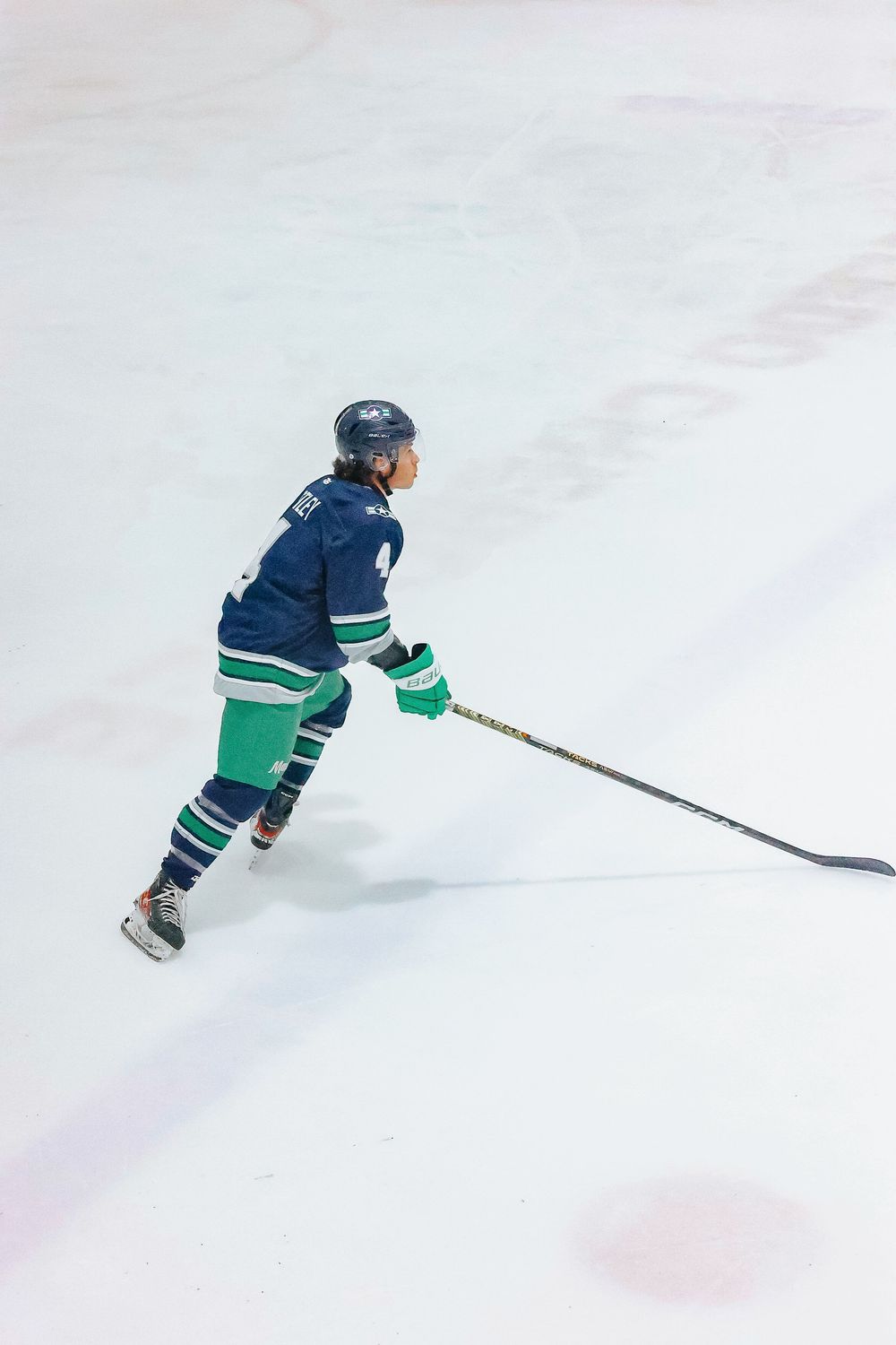 Hockey player in blue and green uniform skating on ice with stick extended during game.
