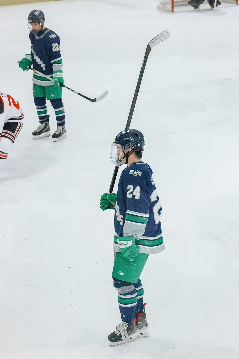 Hockey players in blue and green jerseys positioned on ice during gameplay.